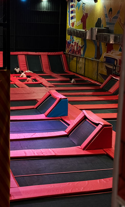 An indoor trampoline park with multiple interconnected trampolines and a few young people enjoying the space.