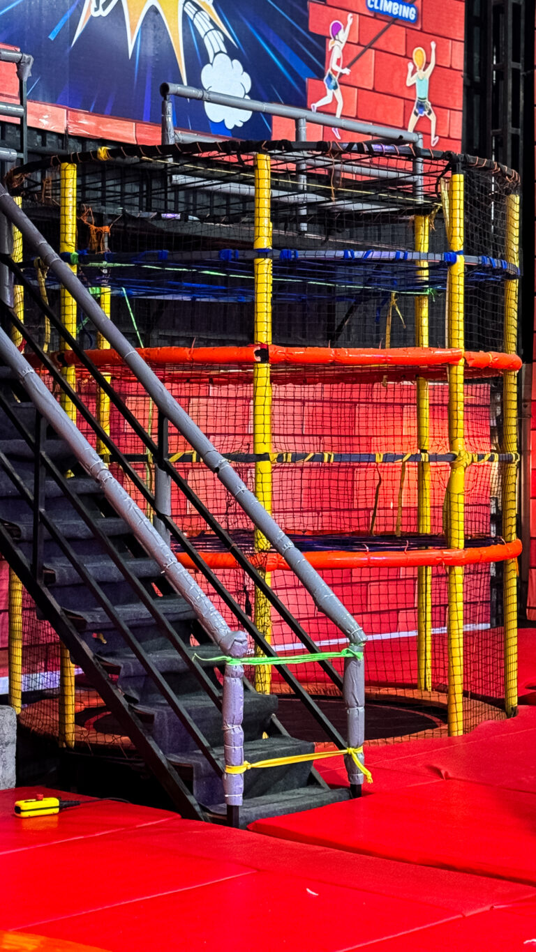 A colorful indoor playground with a climbing structure, stairs, and red mats.