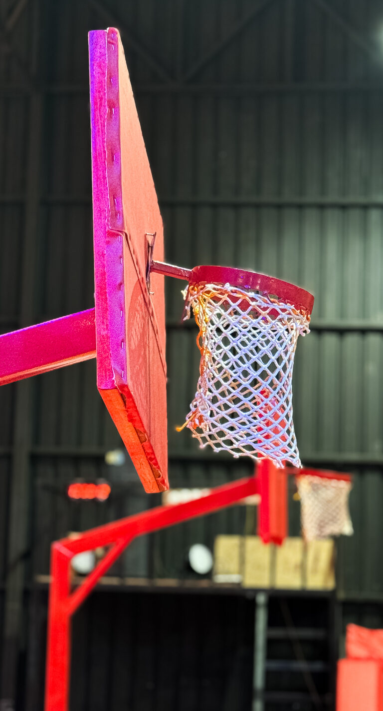 A close-up of a pink basketball backboard and net in an indoor court.