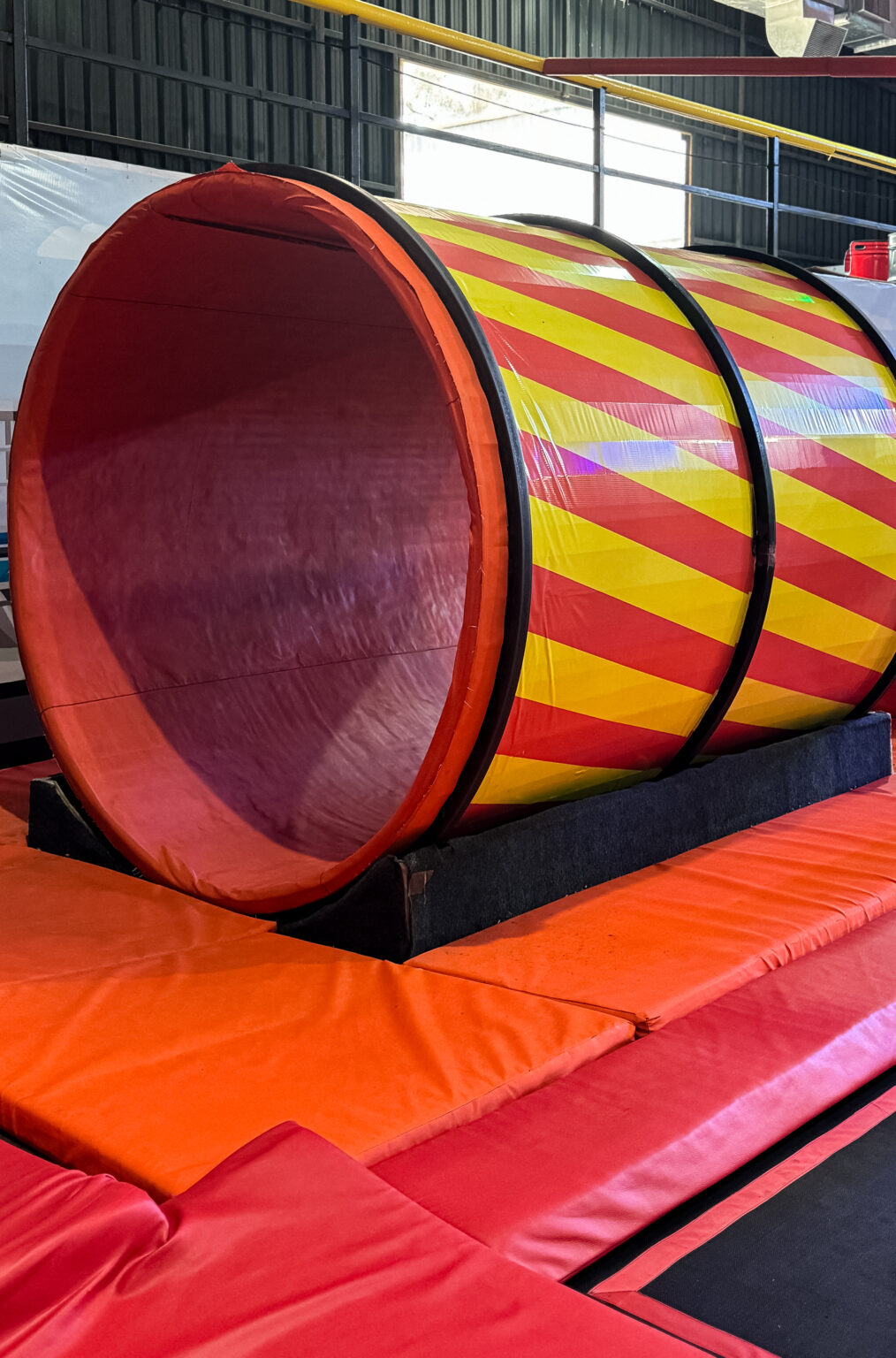 A colorful tunnel on a trampoline park, with red and orange padding.