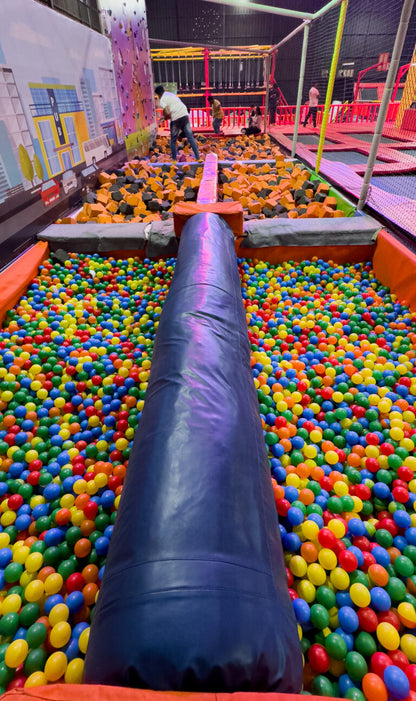 A ball pit filled with colorful balls and a large blue inflatable tube, with people in the background at an indoor adventure park.