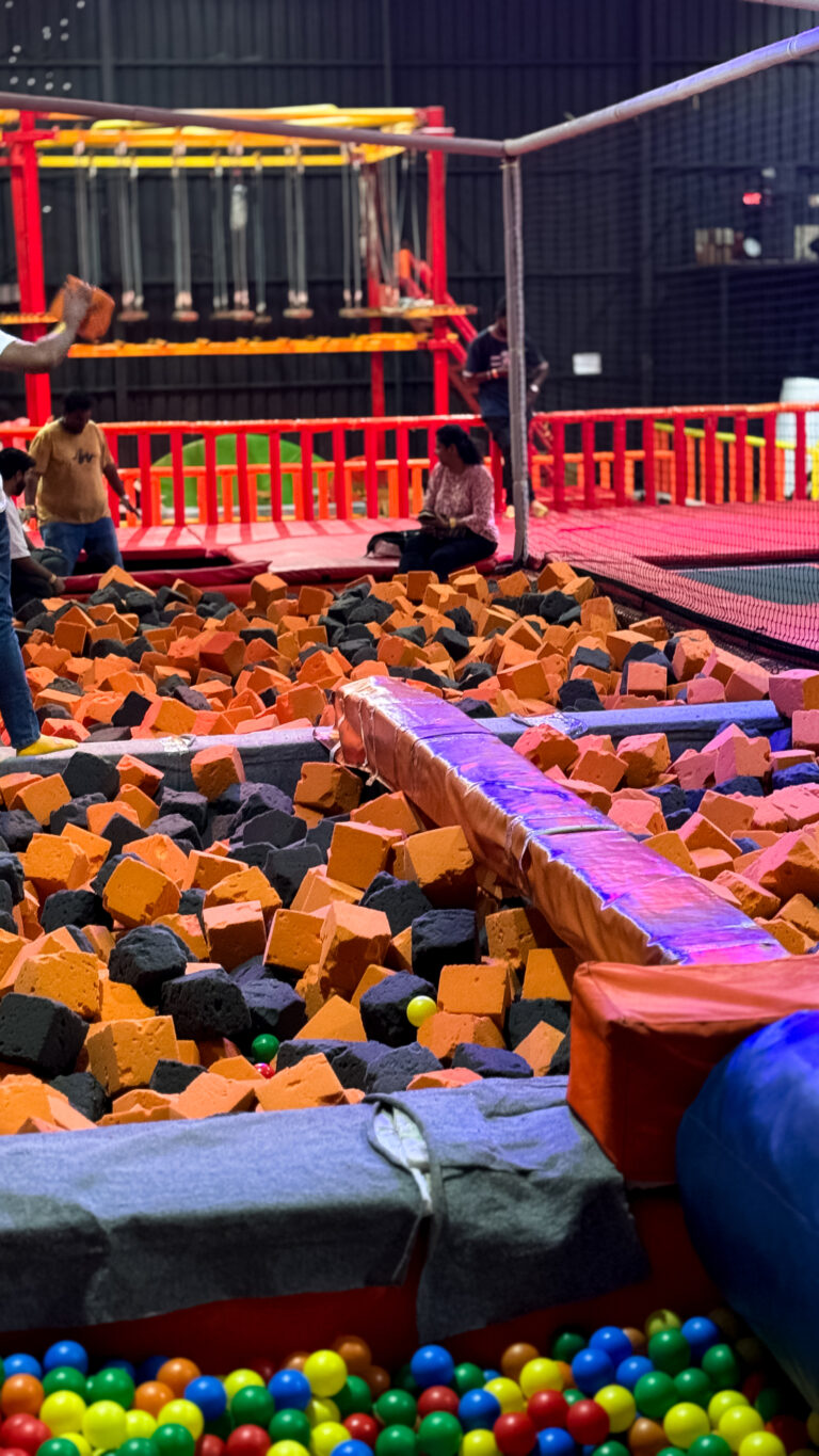A foam pit filled with orange and black foam cubes, with colorful balls at the bottom and people in the background.