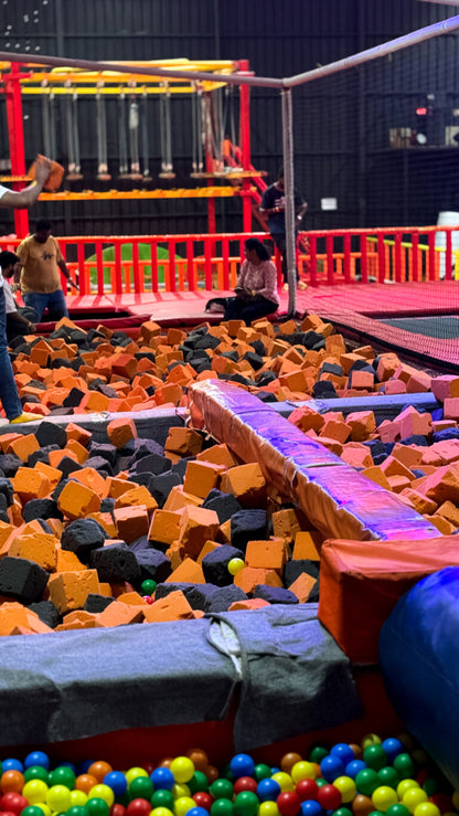 A foam pit filled with orange and black foam cubes, with colorful balls at the bottom and people in the background.