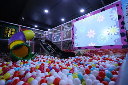 Colorful ball pit with a slide and screen in an indoor playground.