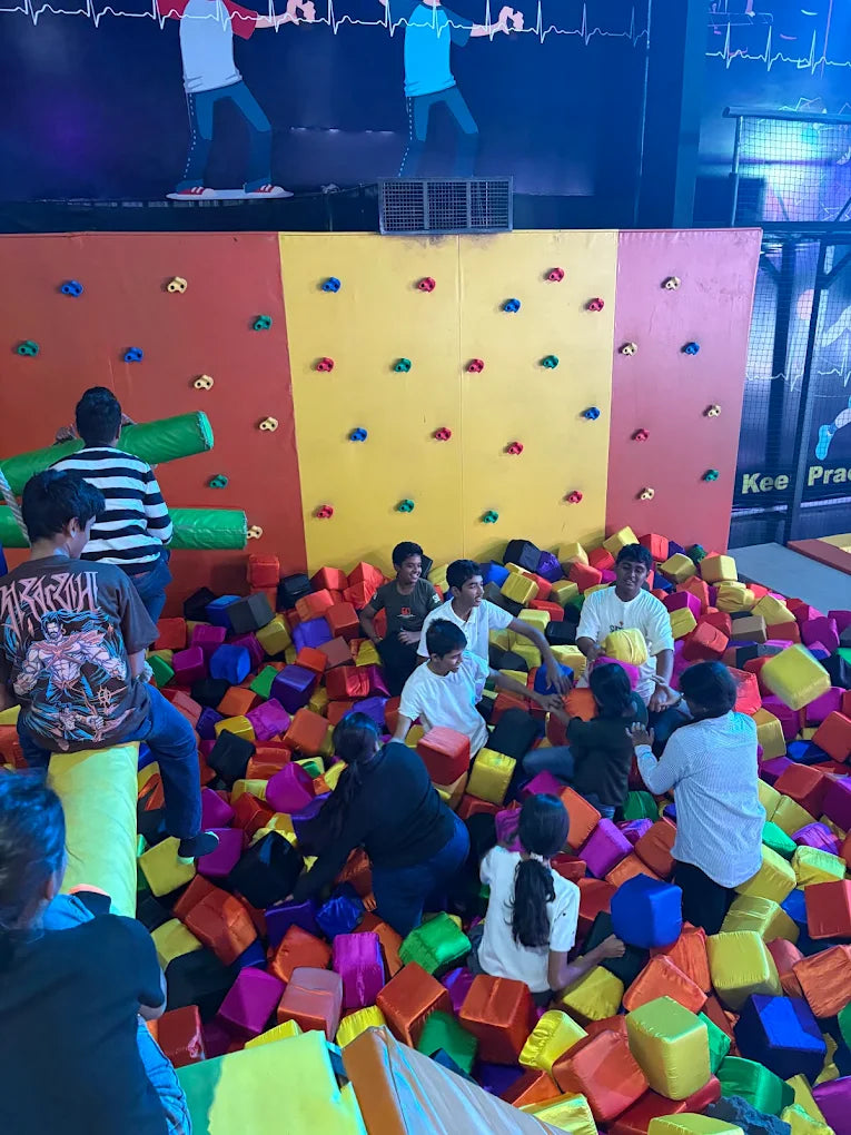 Children play in a foam pit in front of a climbing wall.