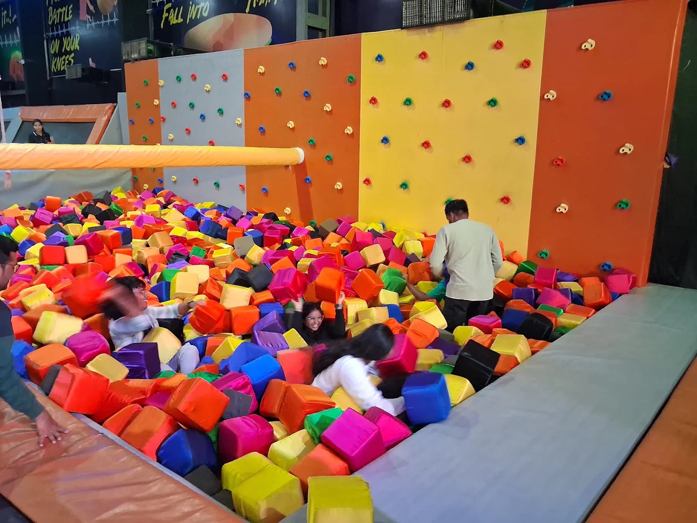 Young people play in a foam pit with a climbing wall in the background.