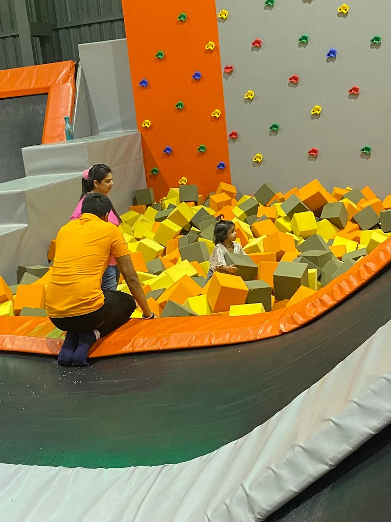 A family enjoys a foam pit at an indoor play area with climbing walls.