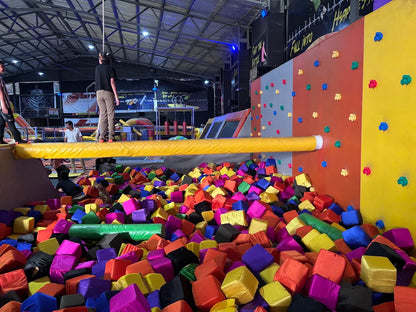 A group of people at a trampoline park, with a foam pit filled with colorful cubes.