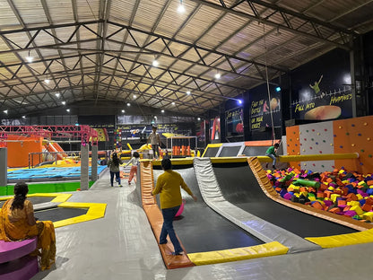 People of various ages enjoy a trampoline park with foam pits and climbing walls.