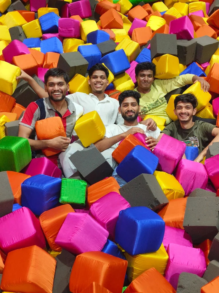 Young men smile while sitting in a foam pit filled with colorful cubes.