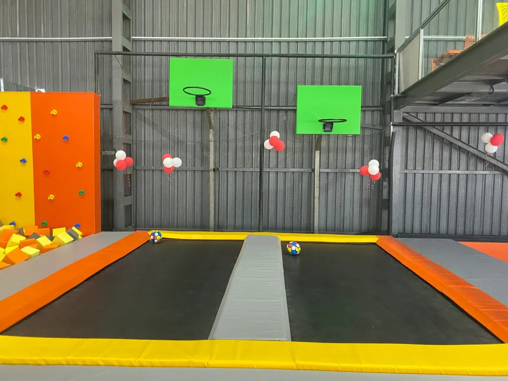 Indoor trampoline park with basketball hoops and colorful foam blocks.