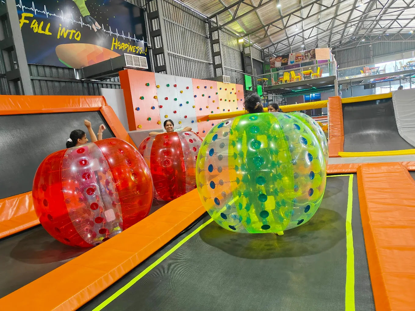 Children play inside large inflatable balls on trampolines at an indoor amusement park.