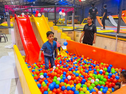 Children play in a ball pit at an indoor trampoline park with slides.