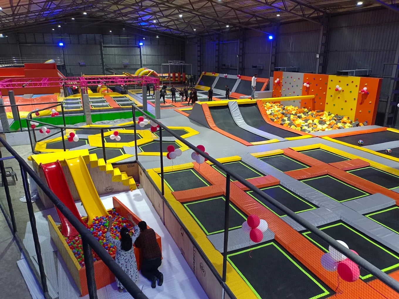 An indoor trampoline park with various trampolines, foam pits, and slides, where young people are enjoying the activities.