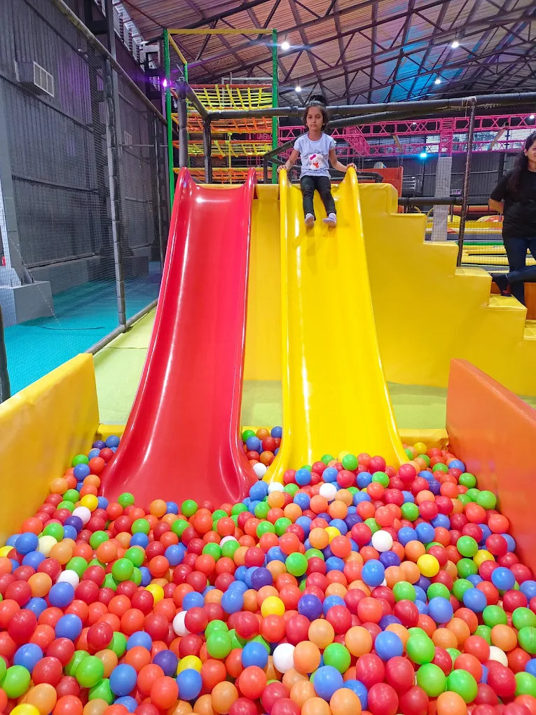 A young girl stands at the top of a yellow slide in a ball pit, ready to play.