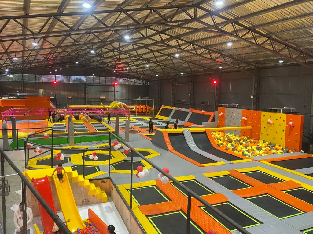 An indoor trampoline park with children and adults jumping and playing on various trampolines and slides.