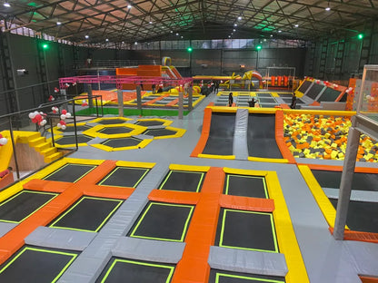 An indoor trampoline park with various trampolines, foam pits, and climbing walls, with people of various ages enjoying the activities.