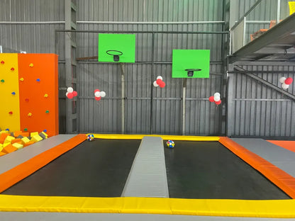 Indoor trampoline park with basketball hoops and colorful foam blocks.