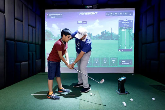 Two people practicing golf indoors with a screen displaying a golf simulation game.
