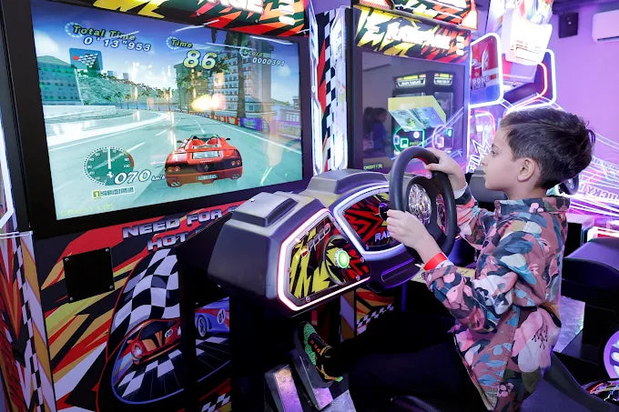 Child playing a racing game on an arcade machine with colorful lights and graphics.