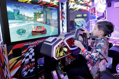 Child playing a racing game on an arcade machine with colorful lights and graphics.