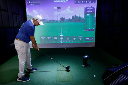 A man practices golf indoors on a simulator, with a large screen displaying his shot data.