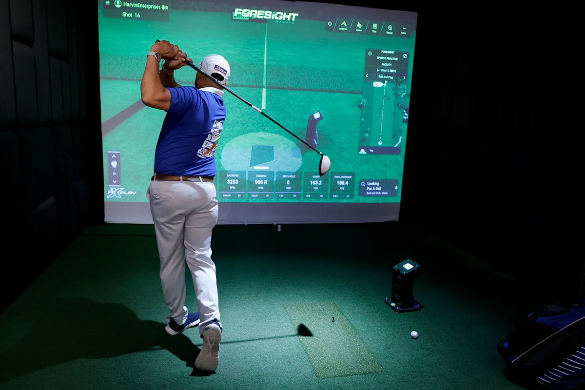 A man plays golf on a simulator, with a large screen displaying his shot data.