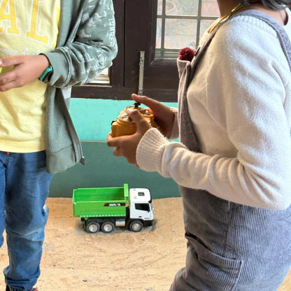 Two children play with a toy dump truck and a remote control.