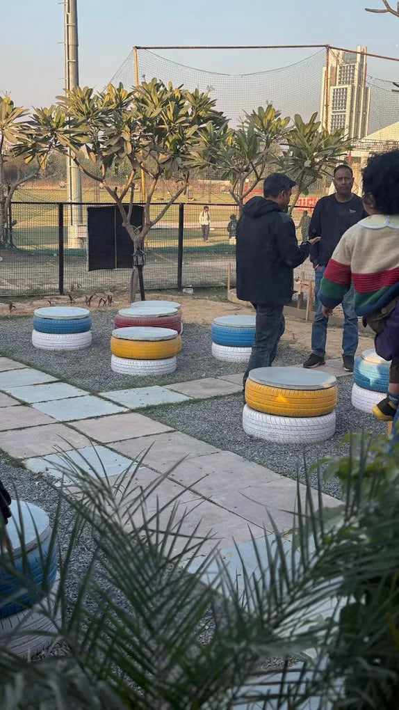 People gather around colorful tire seats in an outdoor seating area.