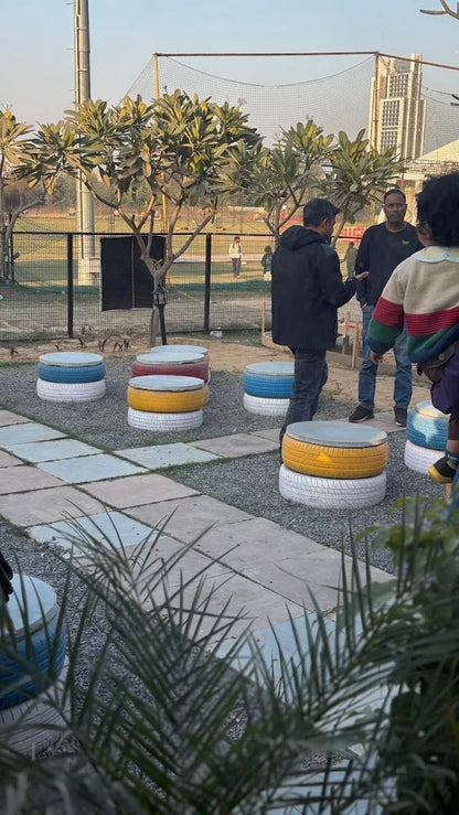 People gather around colorful tire seats in an outdoor seating area.
