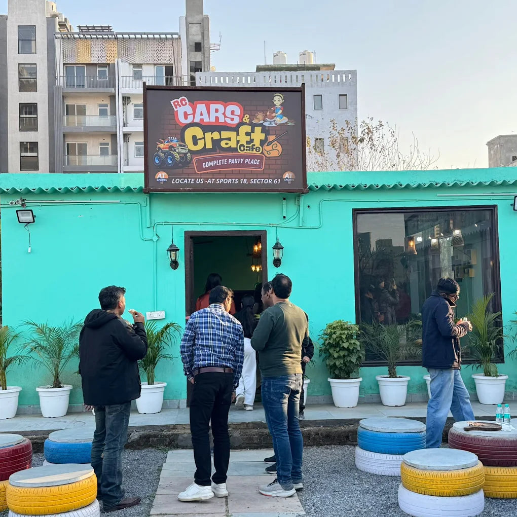 Adults stand outside a teal-colored cafe with a "RC Cars & Craft Cafe" sign.