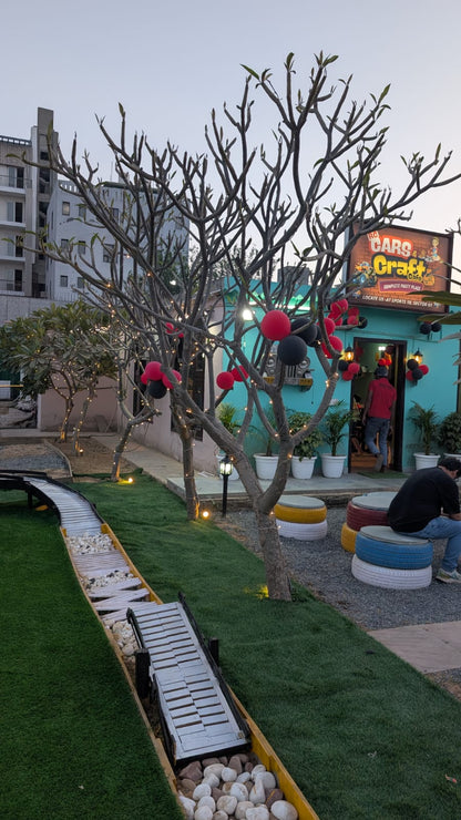 A cafe with outdoor seating decorated with balloons and lights, featuring a miniature railway track.