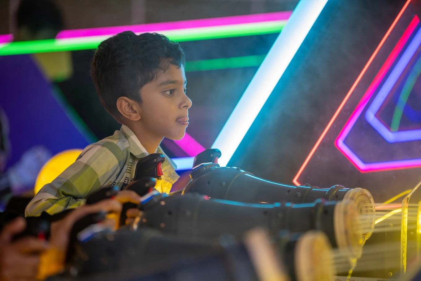 A young boy plays an arcade game, holding a light gun in front of neon lights.