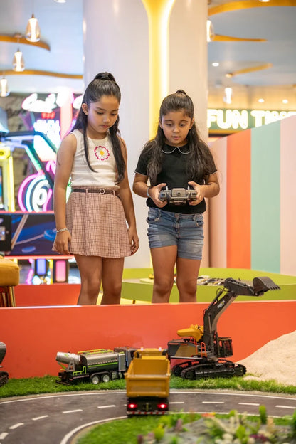 Two young girls play with remote-controlled construction toys in an indoor play area.