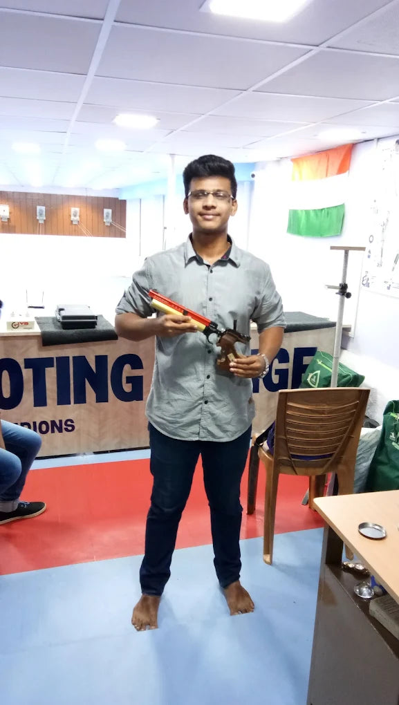 A young man in a grey shirt holds a rifle at a shooting range.