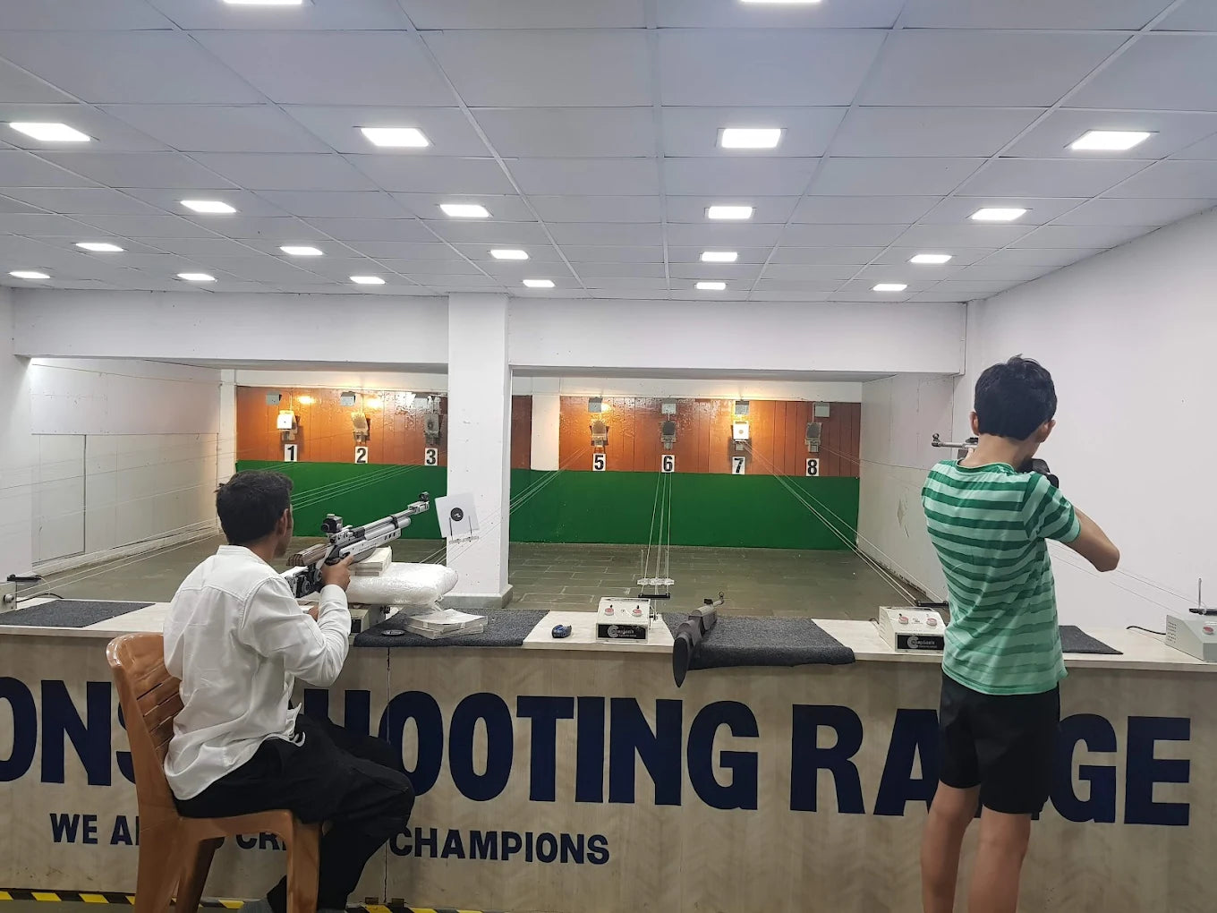 Two young people practice shooting at targets in an indoor shooting range.