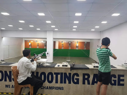 Two young people practice shooting at targets in an indoor shooting range.