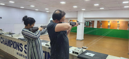 Two adults practice shooting at targets in an indoor range.