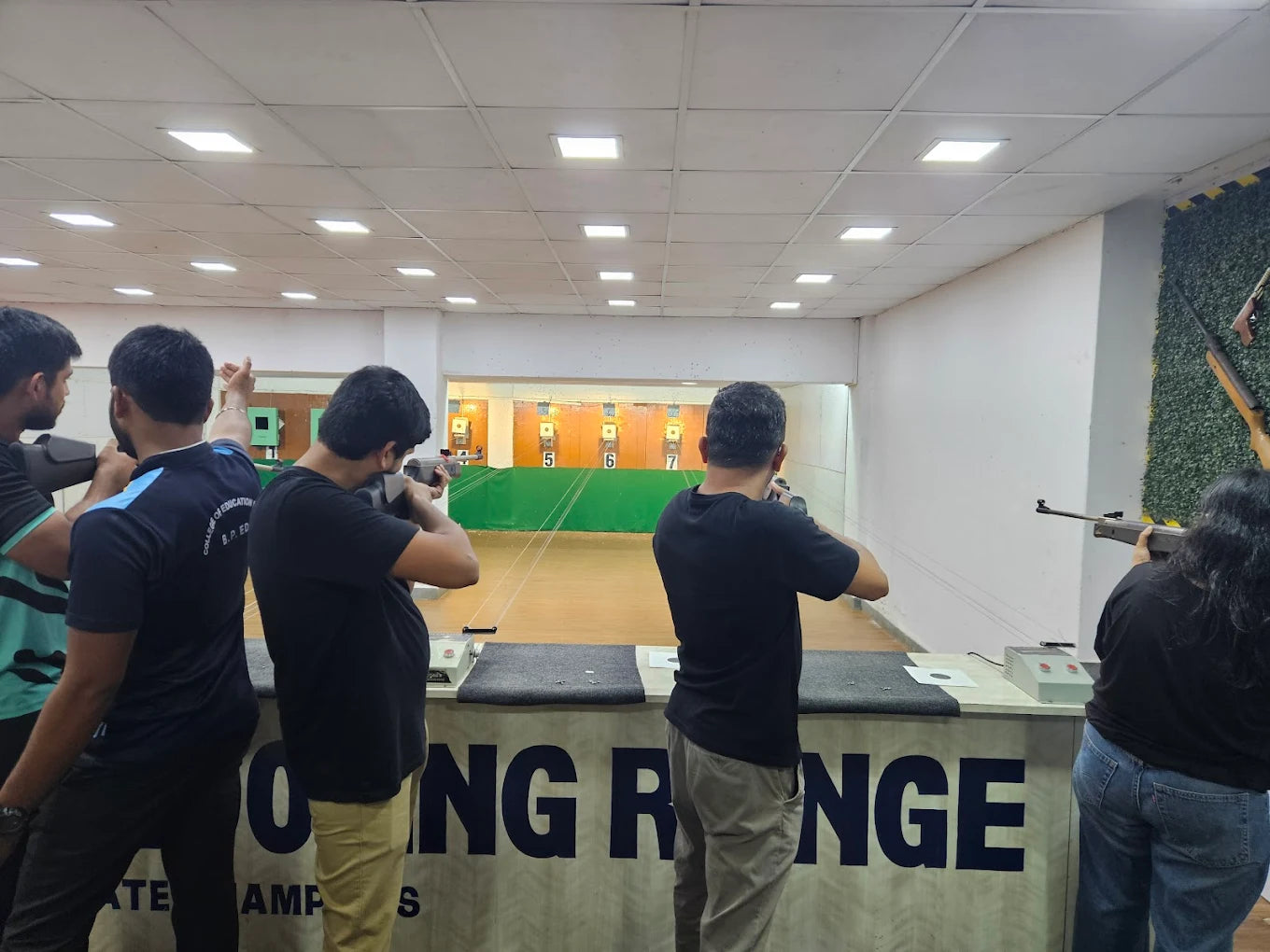 Young adults practice shooting at targets in an indoor range.