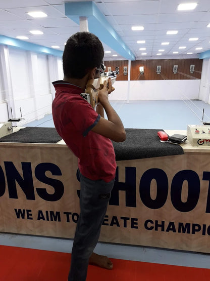 A young person aims a rifle in an indoor shooting range.