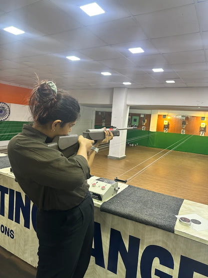 A young woman practices shooting at a target range. She is aiming a rifle at a distant target.