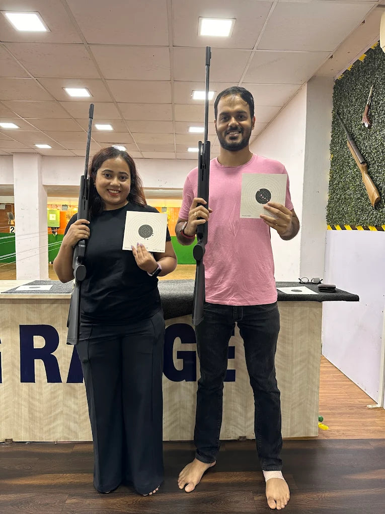 A young man and woman stand with rifles and targets at a shooting range.