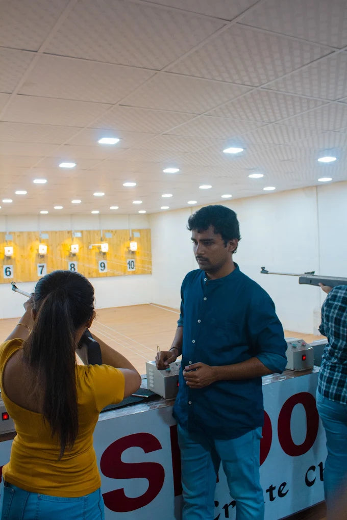 A young woman practices shooting at a range with a male instructor.