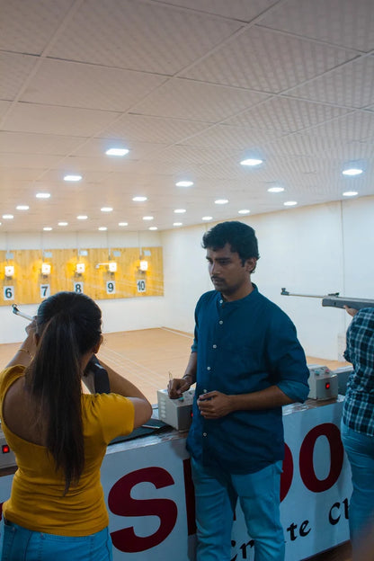 A young woman practices shooting at a range with a male instructor.