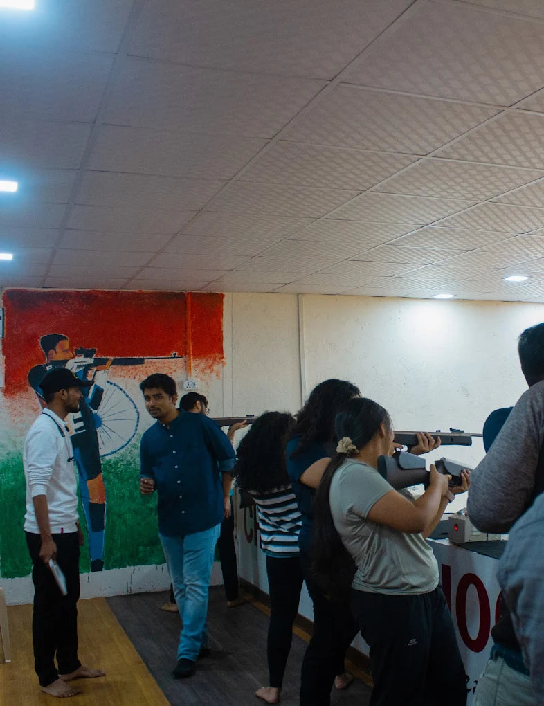 Young adults practice shooting at targets in an indoor range with a mural on the wall.