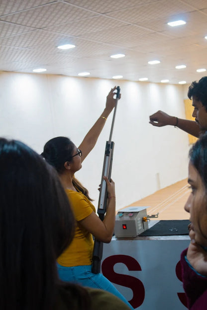 A young woman practices with a rifle at a shooting range, observed by others.