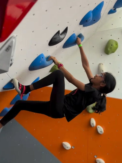 A young person climbs an indoor rock wall, using colorful holds.