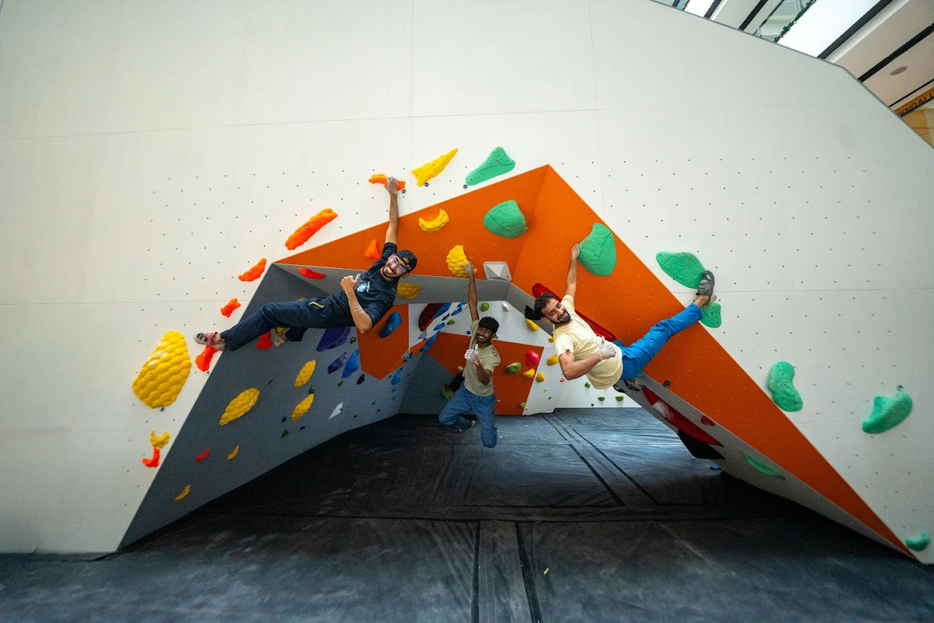 Three young men are bouldering on an indoor climbing wall with colorful holds.