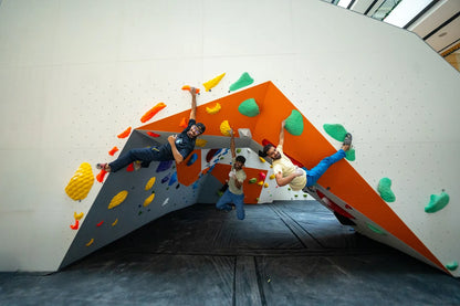 Three young men are bouldering on an indoor climbing wall with colorful holds.