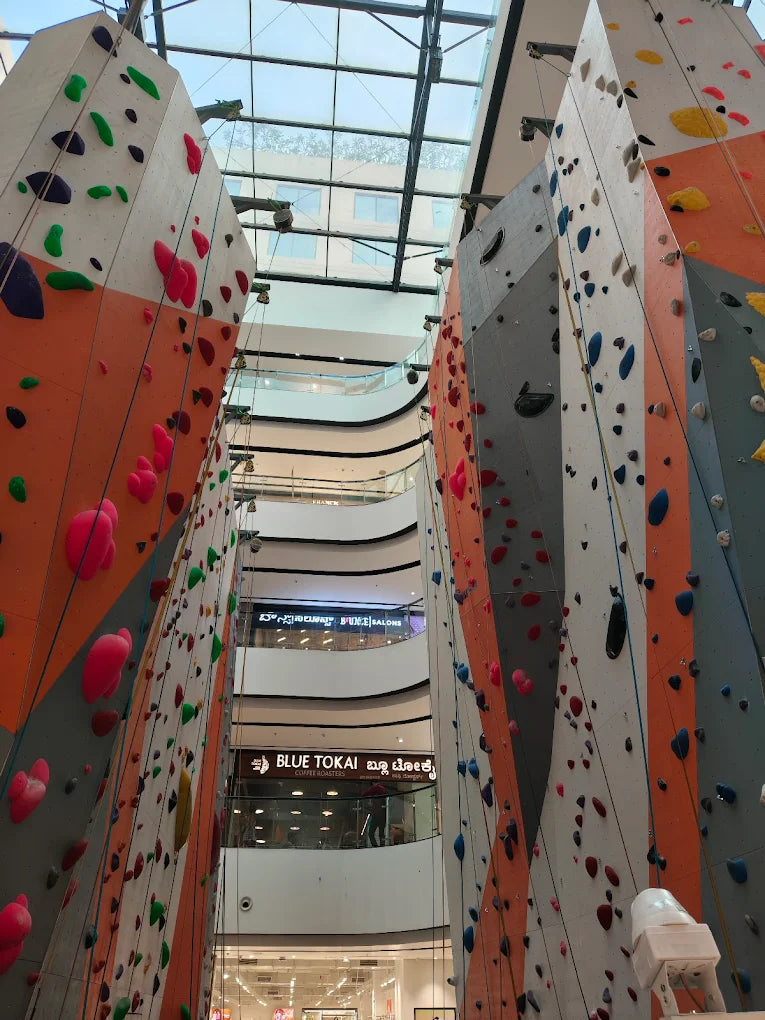 Indoor climbing walls in a mall with people visible on lower levels.